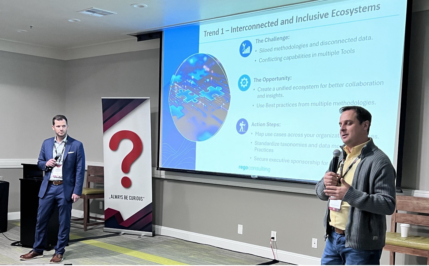 Two presenters speak beside a screen showing “Trend 1 – Interconnected and Inclusive Ecosystems” with challenges, opportunities, and steps